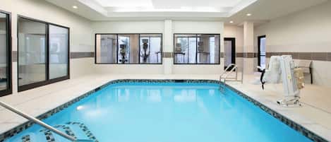 Una piscina interior con paredes de vidrio transparente, suelo de baldosas e iluminación empotrada en el techo.