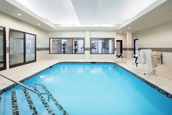 Una piscina interior amb parets de vidre transparent, un terra de rajoles i un sostre amb il·luminació empotrada.