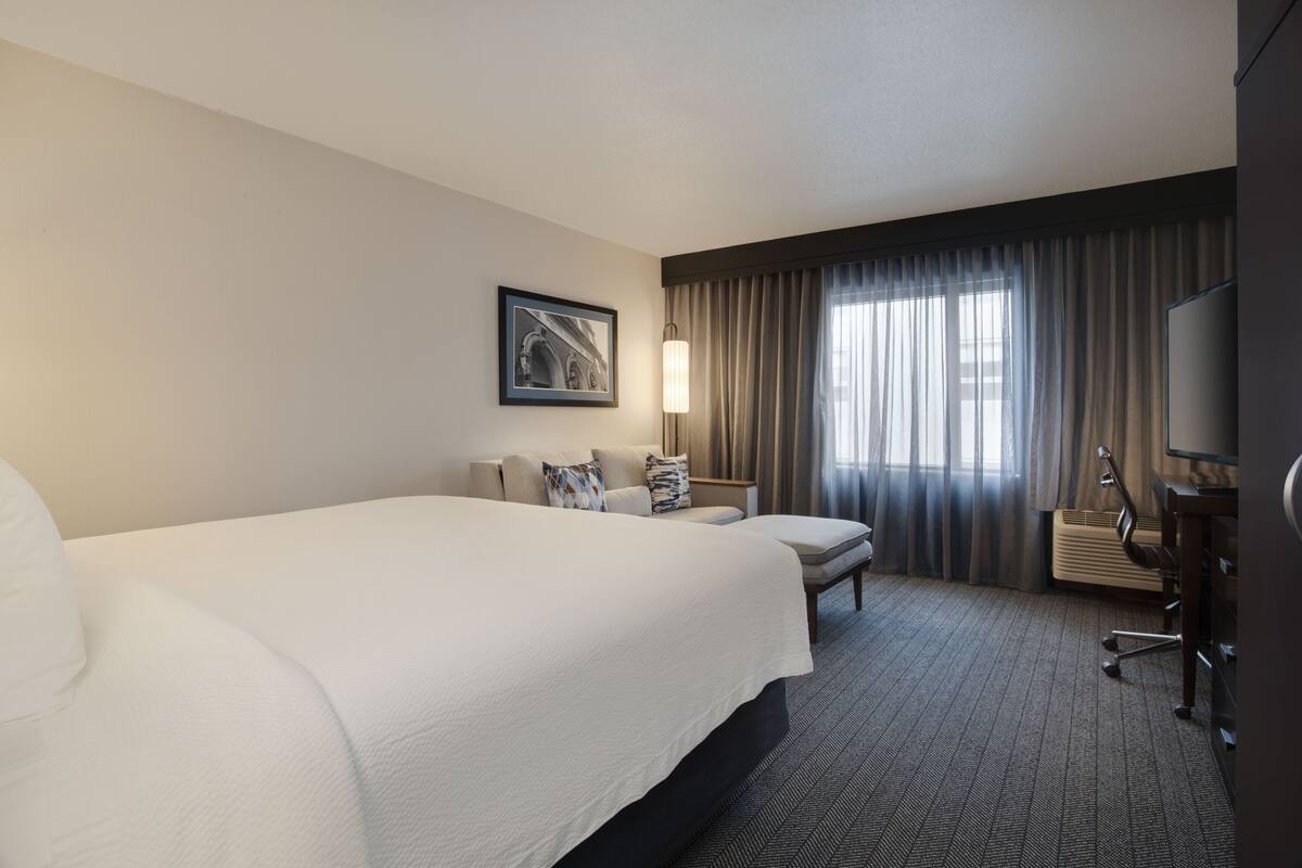 Een hotelkamer met een groot bed, een bureau met stoel, een lamp en een televisietoestel.
