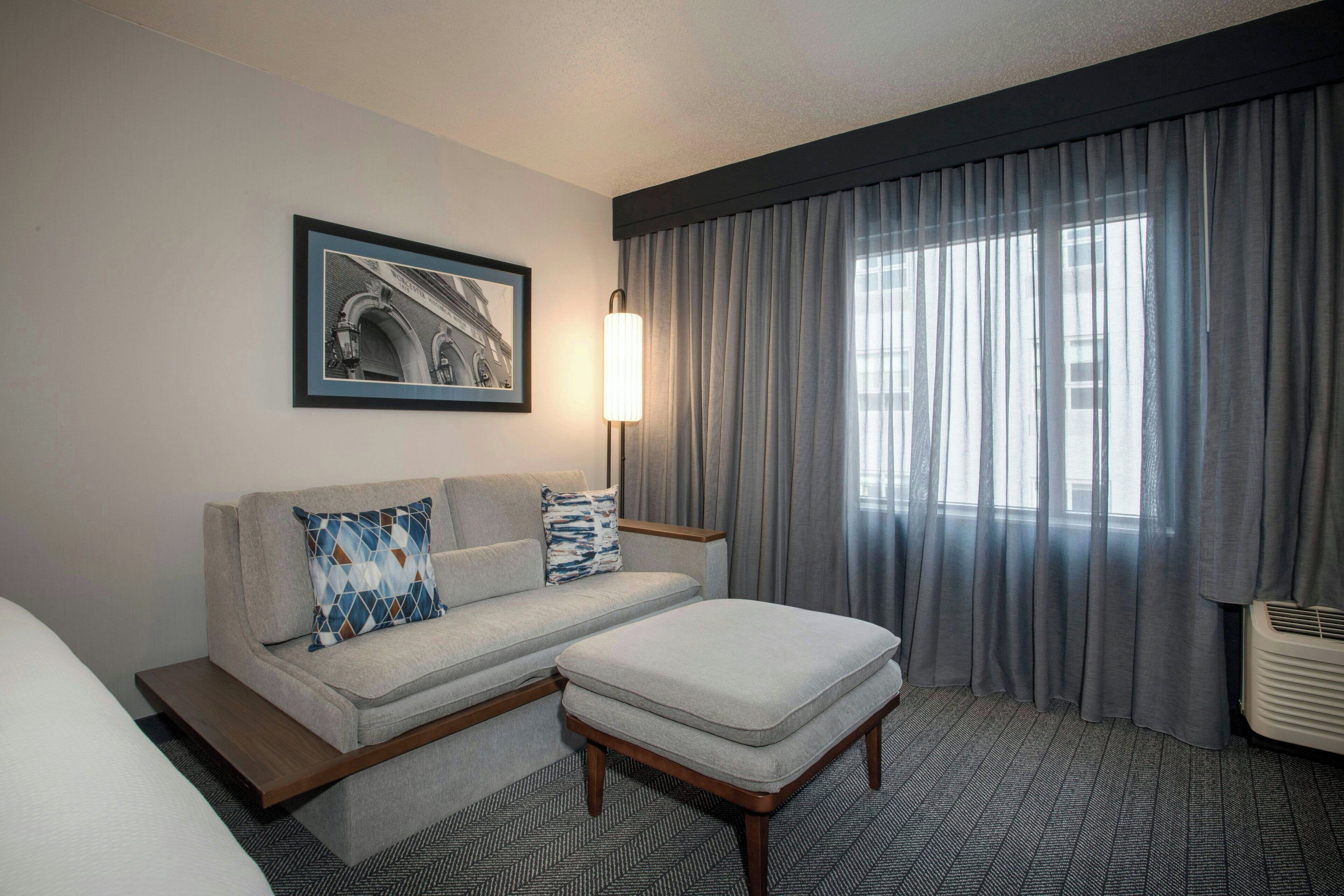 Une chambre d’hôtel avec un canapé, un pouf et un tableau encadré au mur.