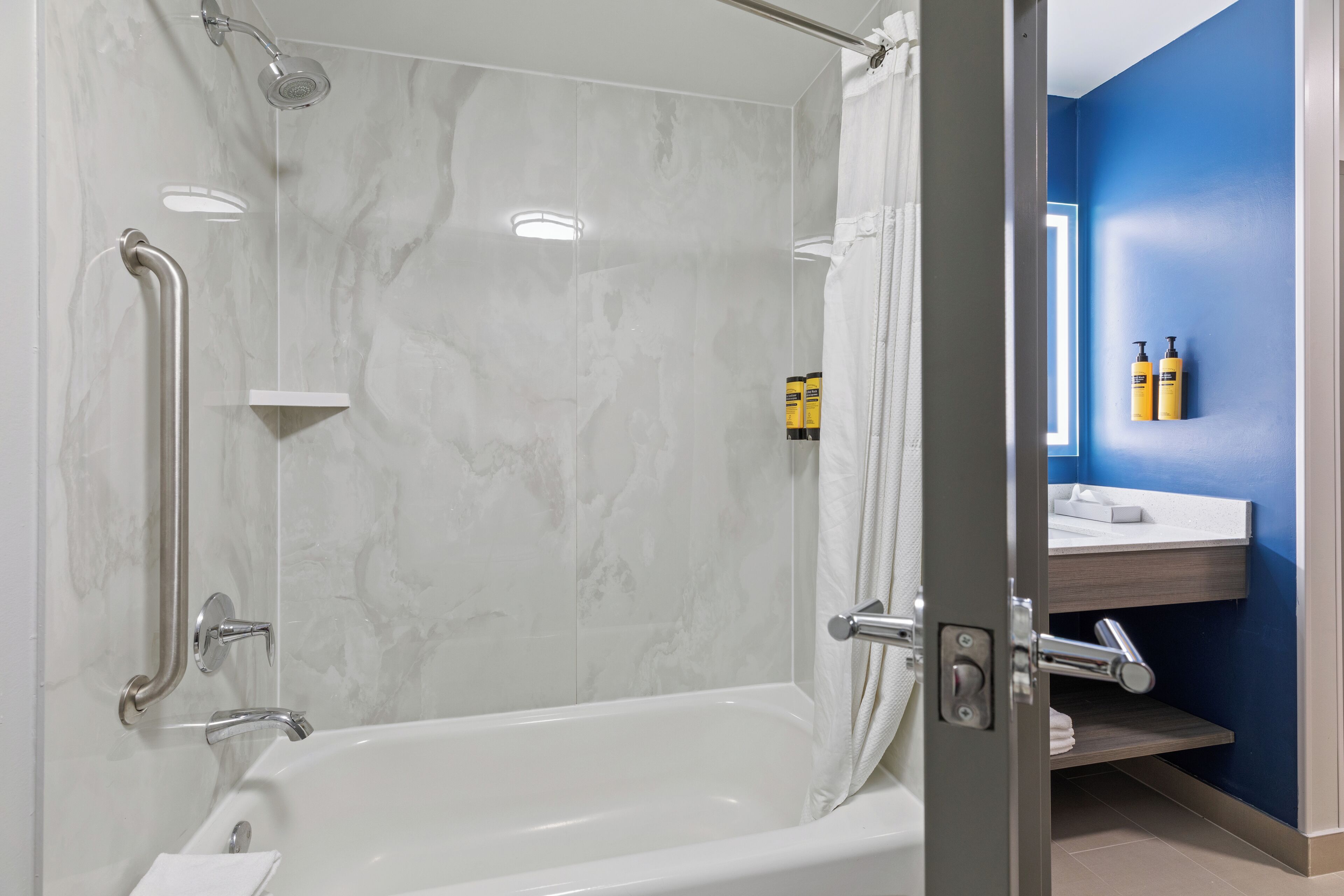 Un baño moderno con ducha a nivel, barras de apoyo y un mueble de tocador con espejo y artículos de aseo.