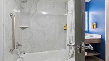 Un baño moderno con ducha a nivel, barras de apoyo y un mueble de tocador con espejo y artículos de aseo.