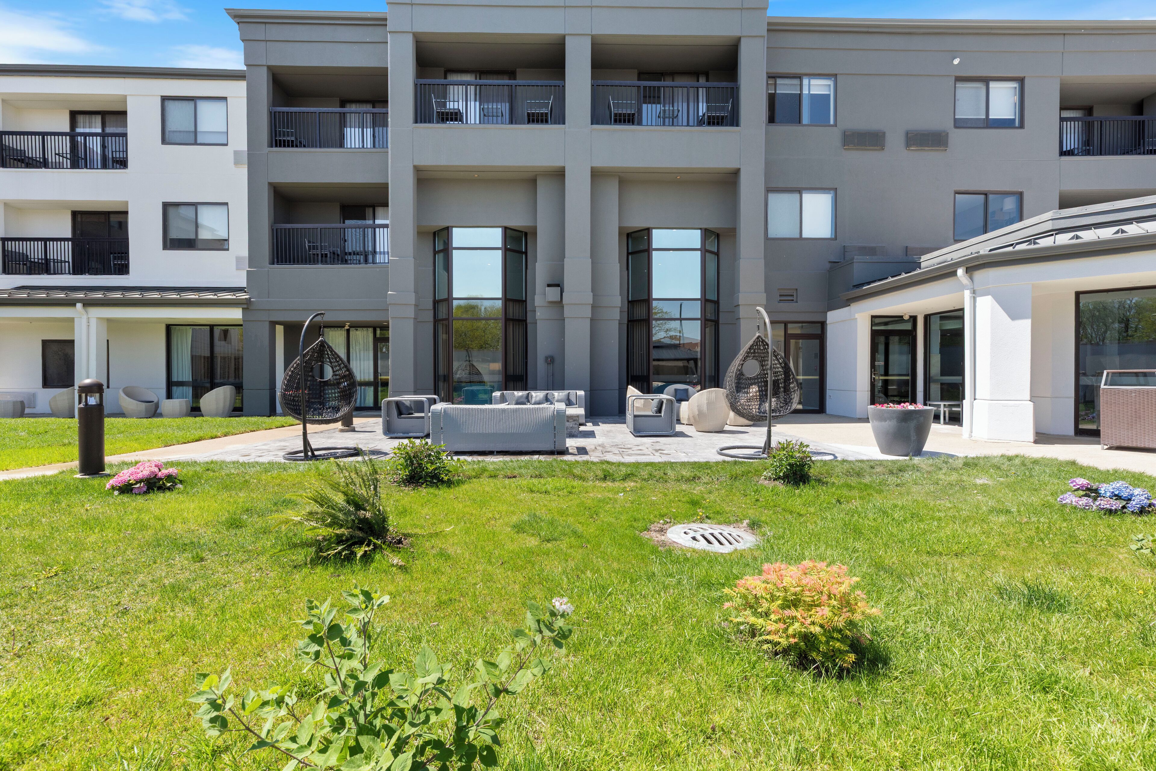 Een modern appartementencomplex met balkons, een binnentuin met buitenmeubilair en een verzorgd gazon.