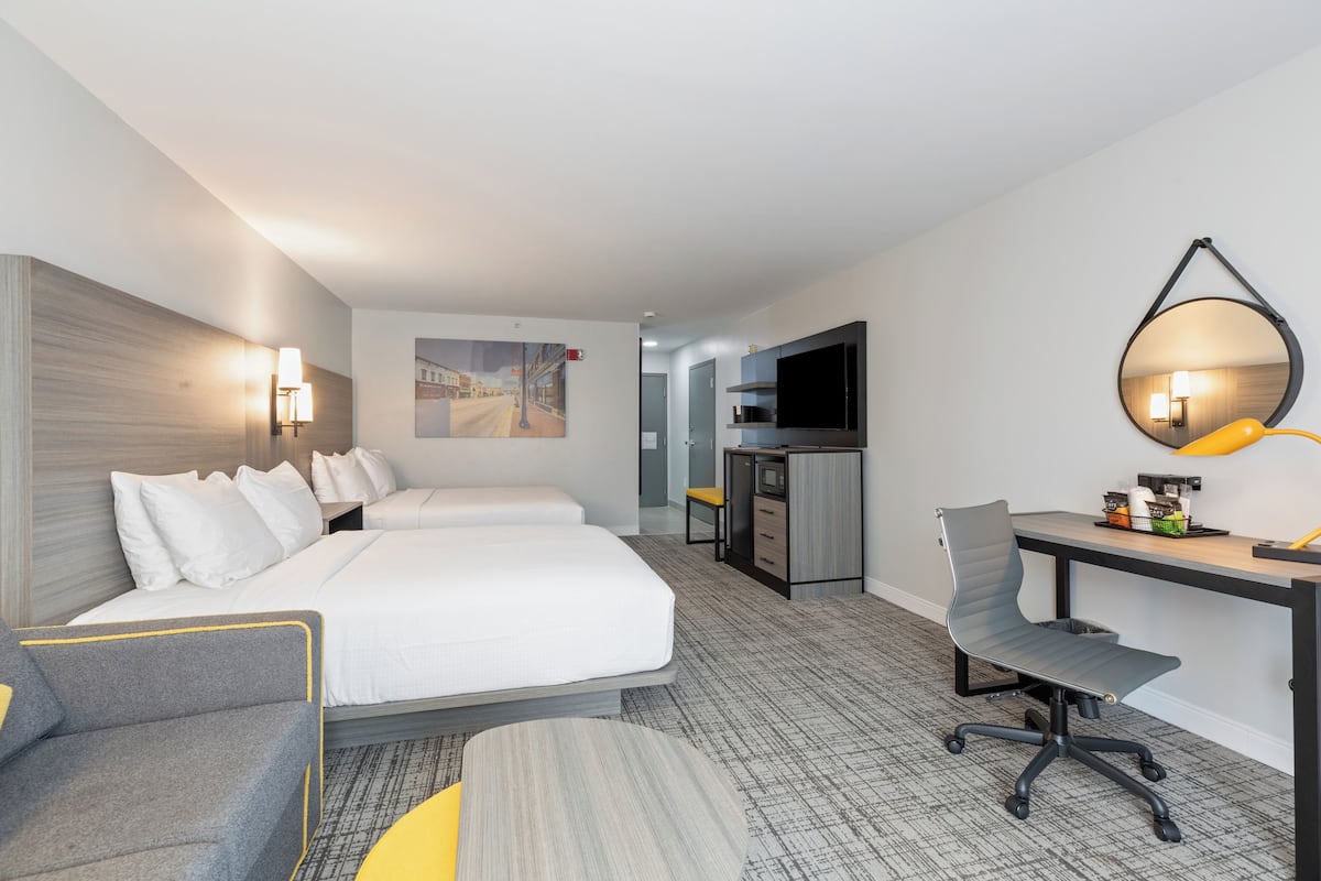 Una habitación de hotel con cama, escritorio, silla, televisor y espejo.
