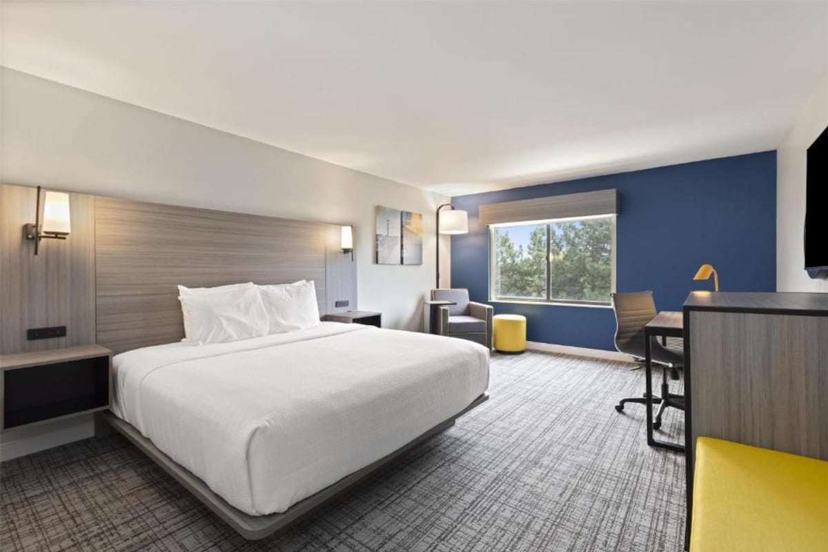 Ein Hotelzimmer mit einem großen Bett, einem Schreibtisch, einem Sessel und einem Fernseher.