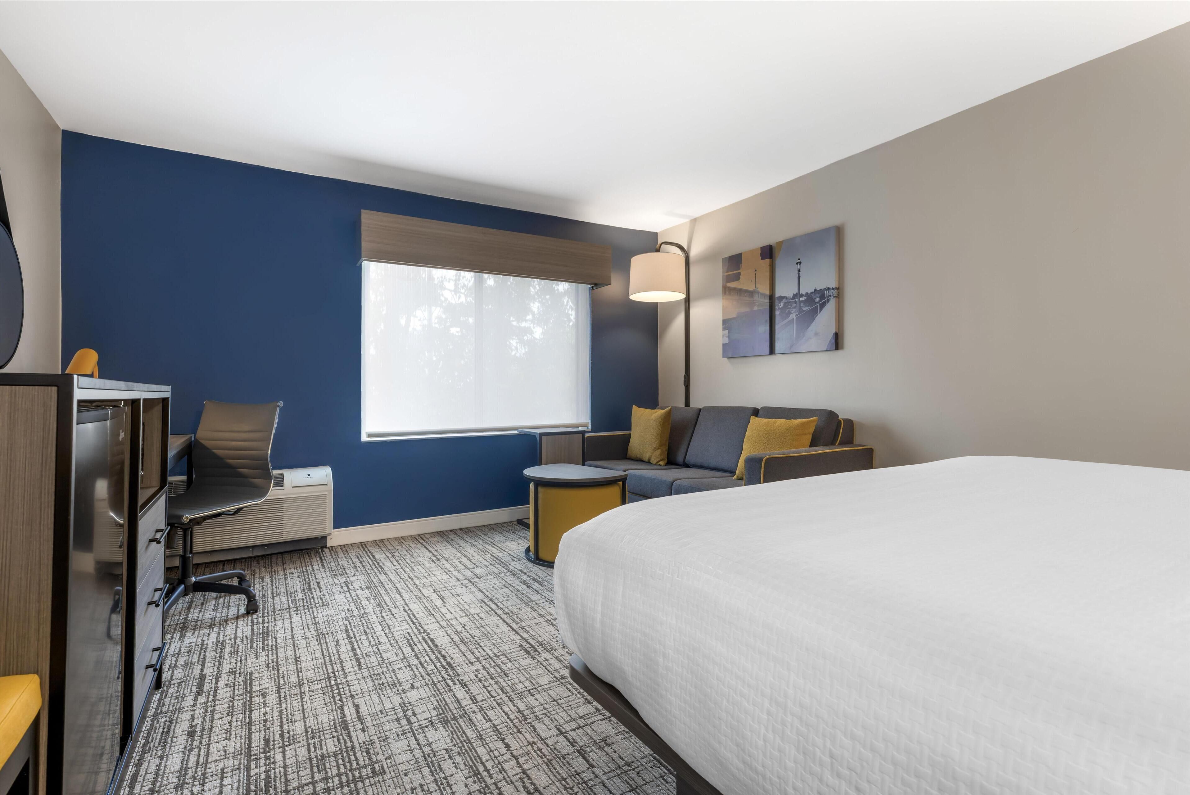 A hotel room with a bed, a desk, a chair, a sofa, and a small table.
