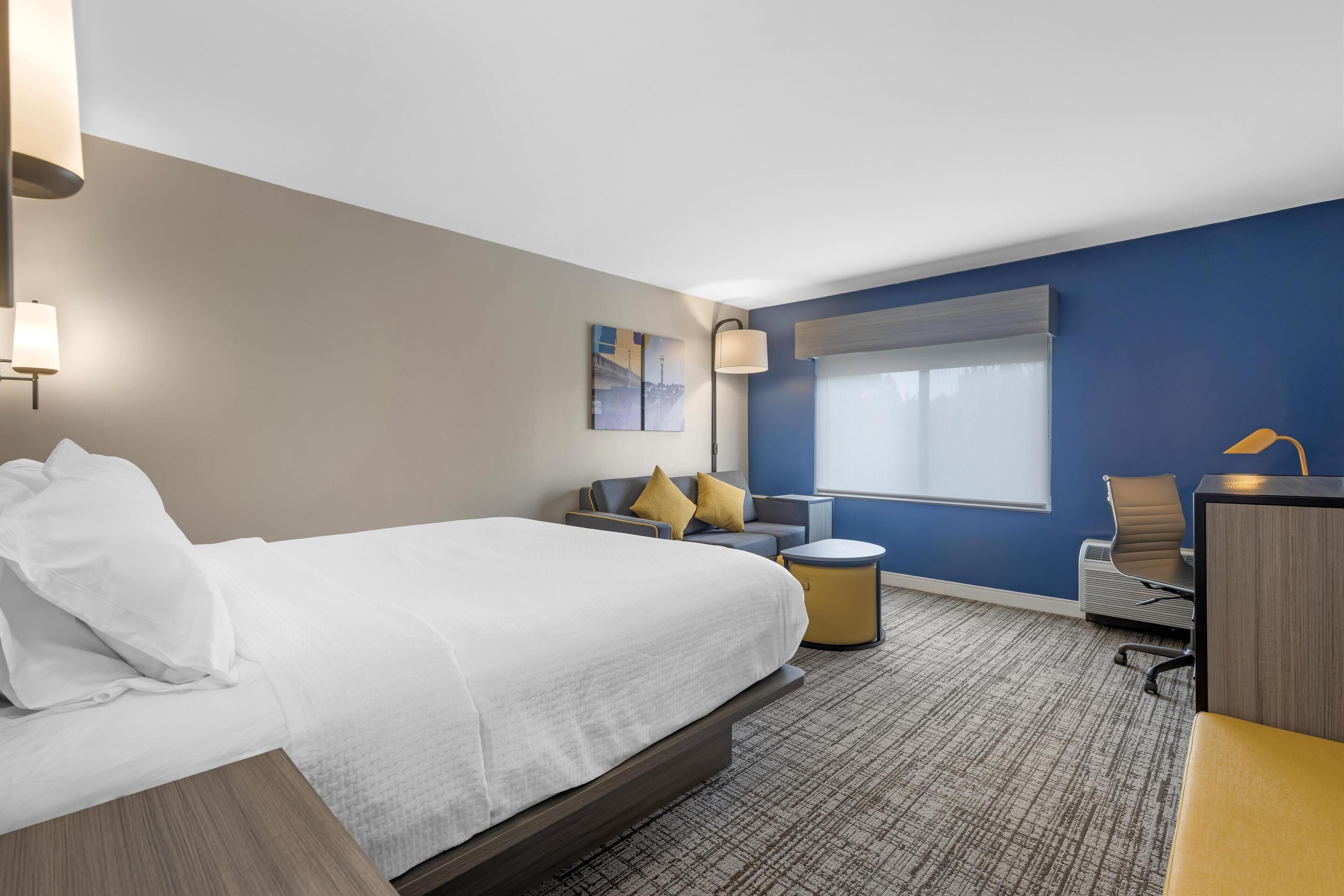 A hotel room with a bed, a desk, a chair, a small table, and a window.