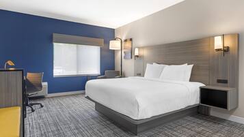Habitación de hotel con una cama grande, un escritorio con silla, una ventana e iluminación en la pared.