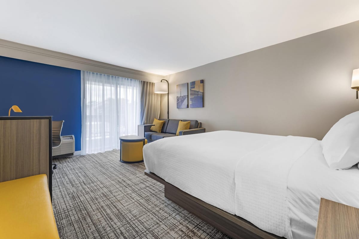 Habitación de hotel con una cama grande, un escritorio, una silla, una mesita y una ventana con cortinas.
