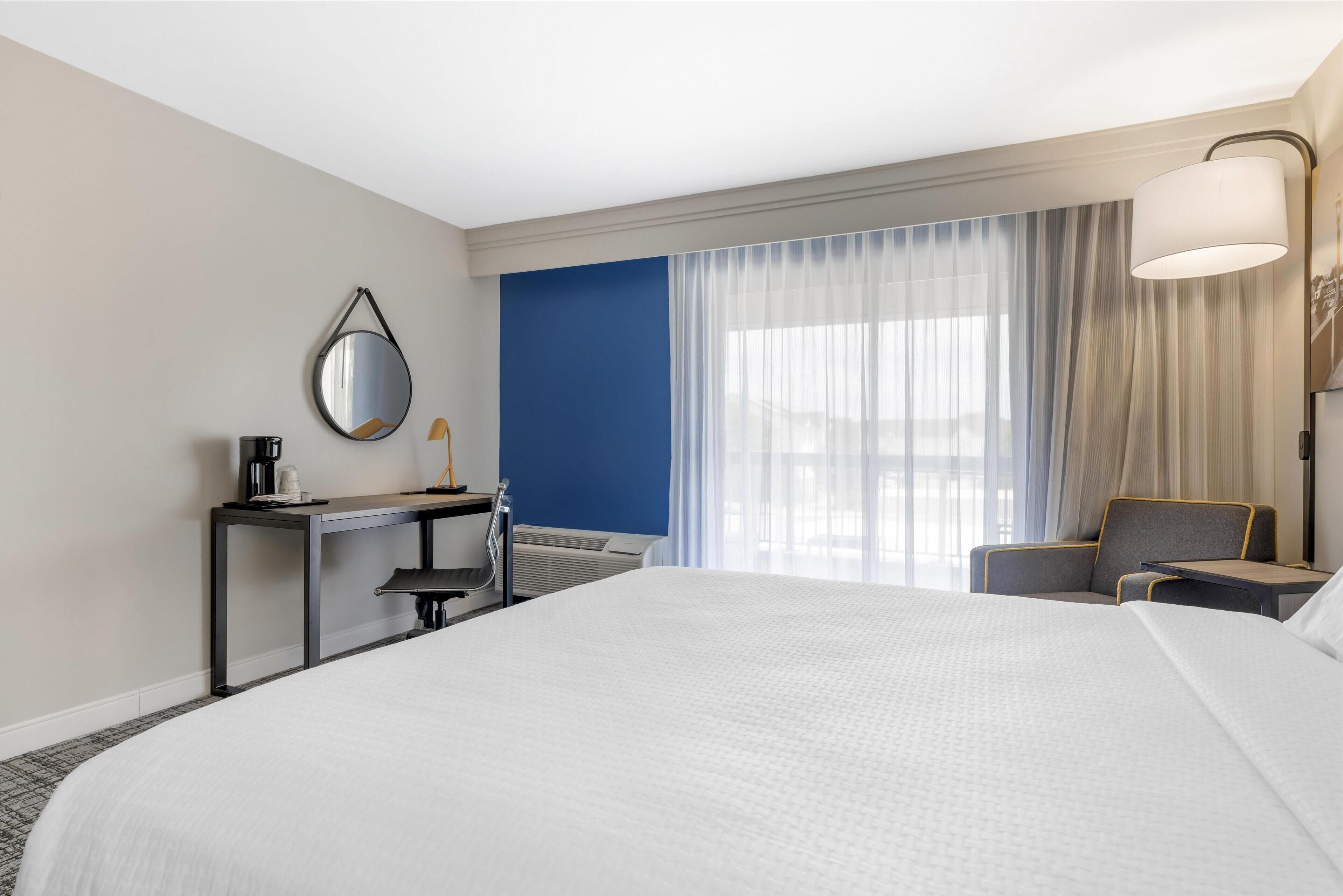 Una habitación de hotel con una cama grande, un escritorio con espejo, una silla y una lámpara.