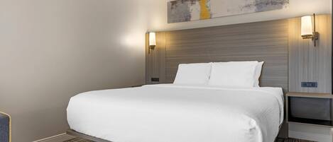 Una habitación de hotel moderna con una cama grande, un cabecero con iluminación integrada, una obra de arte colgada en la pared y una mesita de noche con lámpara.
