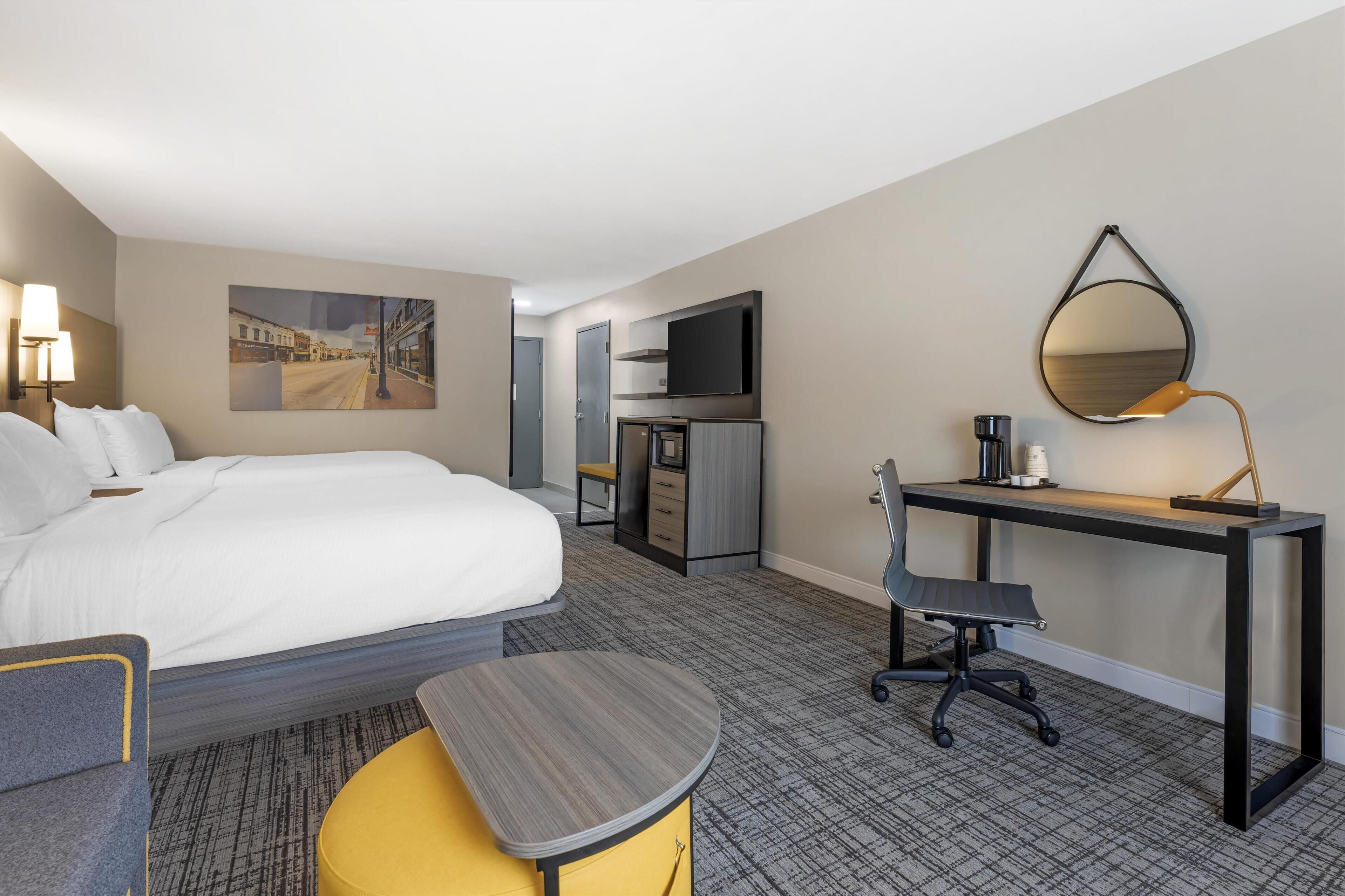 A hotel room with a bed, a desk, a chair, a desk lamp, a flat-screen TV, and a painting on the wall.