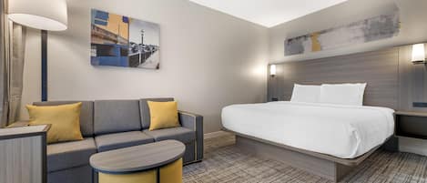 A modern hotel room with a large bed, a sofa, a small table, and a lamp.
