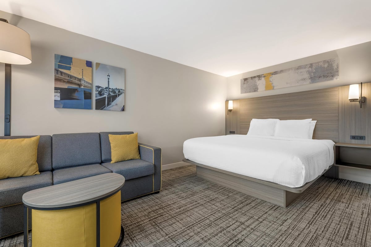 Habitación de hotel con una cama, un sofá, una mesita y dos lámparas de pared.