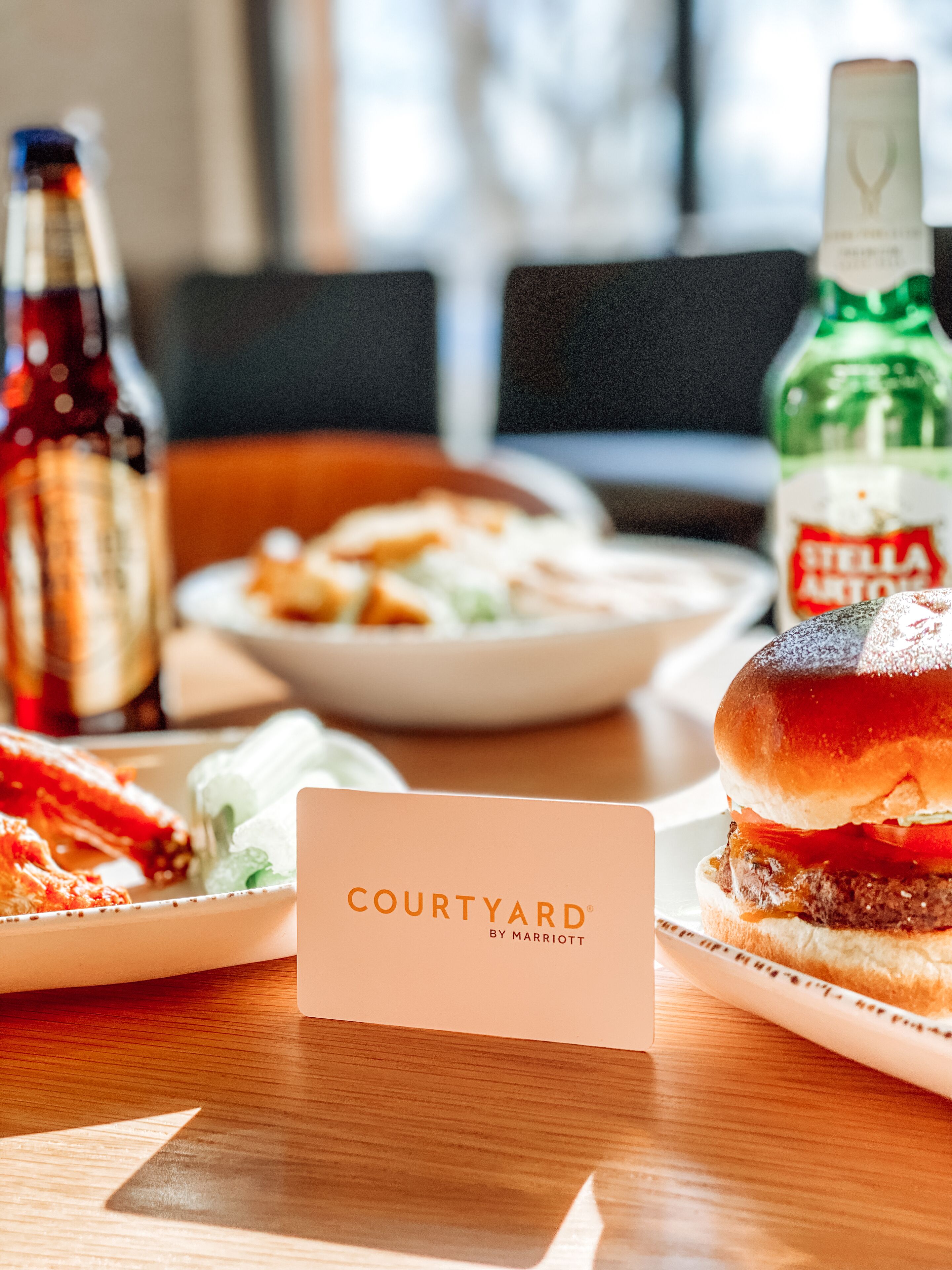 A table with a burger, a plate of food, and two bottles of beverages. A sign with the text "COURTYARD BY MARRIOTT" is in the foreground.