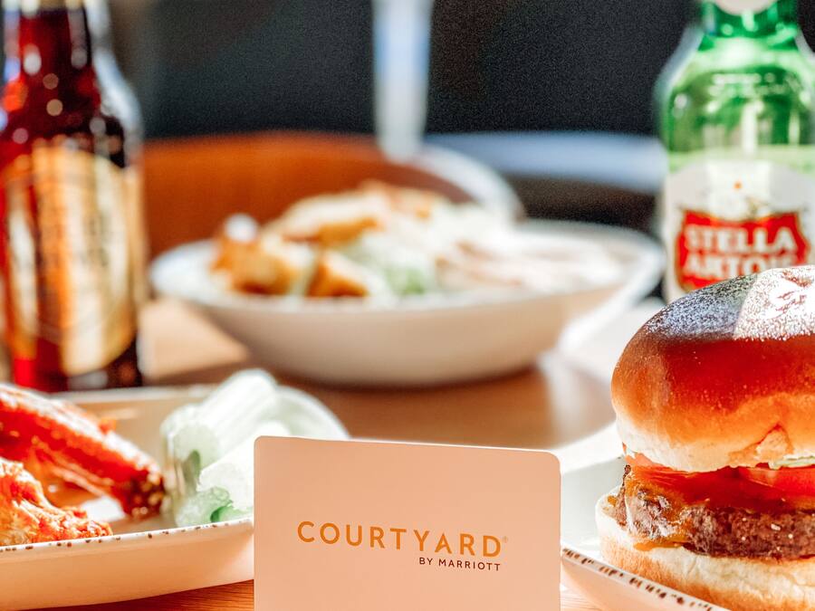A table with a burger, a plate of food, and two bottles of beverages. A sign with the text "COURTYARD BY MARRIOTT" is in the foreground.