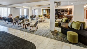 A spacious hotel lobby with multiple seating areas, a bar, and a kitchen visible in the background. - Courtyard Chicago St. Charles (St. Charles)