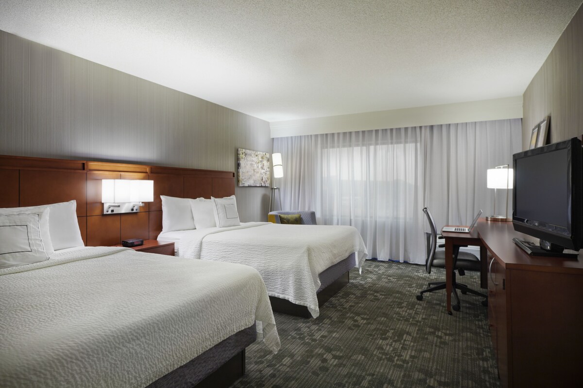 A hotel room with two beds, a desk with a computer, a TV, and a lamp.