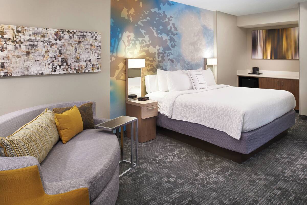 Una habitación de hotel con una cama grande, un sofá, un escritorio y una obra de arte en la pared.