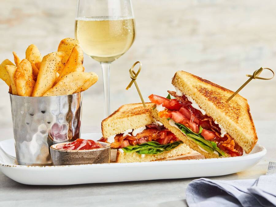 A plate with a grilled sandwich, a glass of white wine, and a container of seasoned fries.
