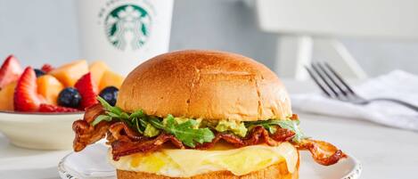 Un sándwich de desayuno en un plato, con una taza de Starbucks al fondo.