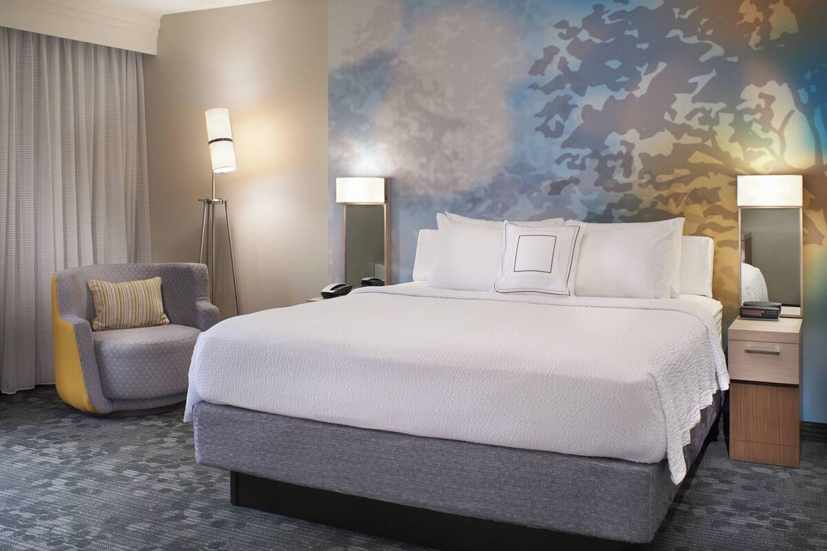 Habitación de hotel con una cama grande, una silla, una mesita de noche y una pared con estampado de camuflaje.