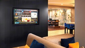 Un hall d’hôtel moderne doté d’un grand écran numérique, d’un espace salon avec des coussins à motifs et d’un comptoir d’accueil.