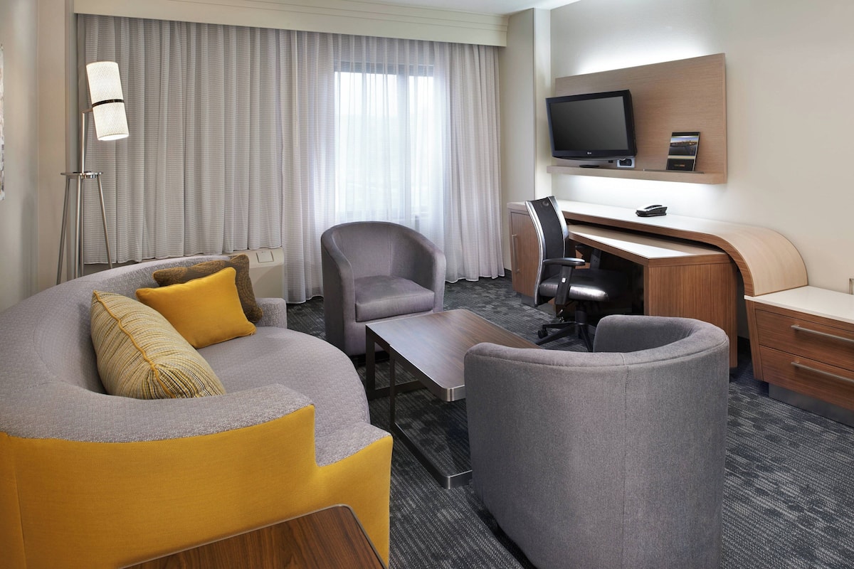 Una habitación de hotel moderna con un sofá curvo, un escritorio, una silla y un televisor de pantalla plana.