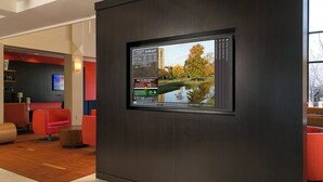 A modern hotel lobby with a digital display, red seating, and a wooden floor.