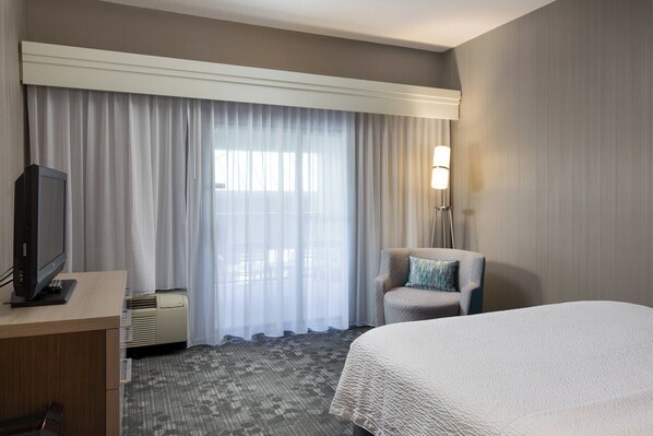 Una habitación de hotel con una cama, un escritorio con televisor, una silla y una lámpara.