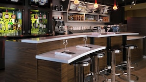 A modern bar area with a curved counter, multiple stools, and overhead lighting.