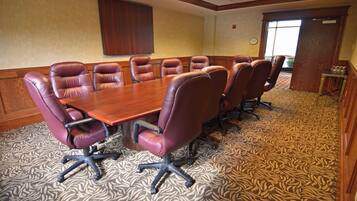 A conference room with a large wooden table surrounded by leather chairs, patterned carpet, wooden paneling, and a window with a view.