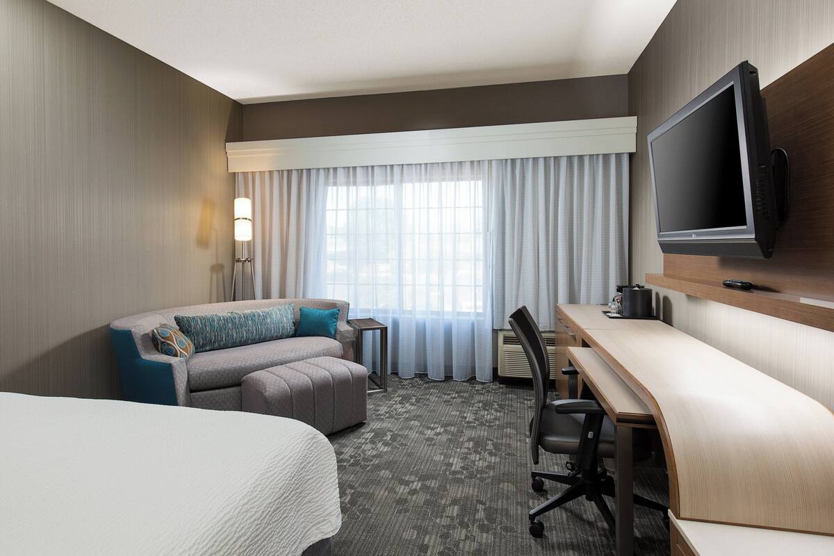 A hotel room with a bed, a sofa, a desk, a chair, a television, and a window with curtains.