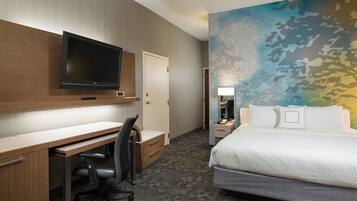 Habitación de hotel con televisor de pantalla plana sobre un escritorio de madera, cama con sábanas blancas y un mural en la pared.