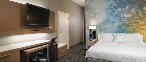 Une chambre d’hôtel dotée d’un téléviseur à écran plat fixé au-dessus d’un bureau en bois, d’un lit avec du linge de lit blanc et d’une fresque murale.