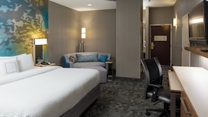 A hotel room with a large bed, a desk, a chair, a lamp, and a mirror.