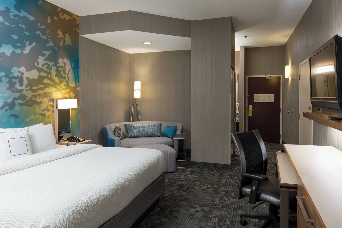 A hotel room with a large bed, a desk, a chair, a lamp, and a mirror.