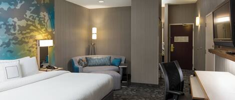 A hotel room with a large bed, a desk, a chair, a lamp, and a mirror.