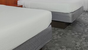 Habitación de hotel con dos camas, cabecero de madera, televisor de pantalla plana, lámpara y un ventanal con cortinas translúcidas.