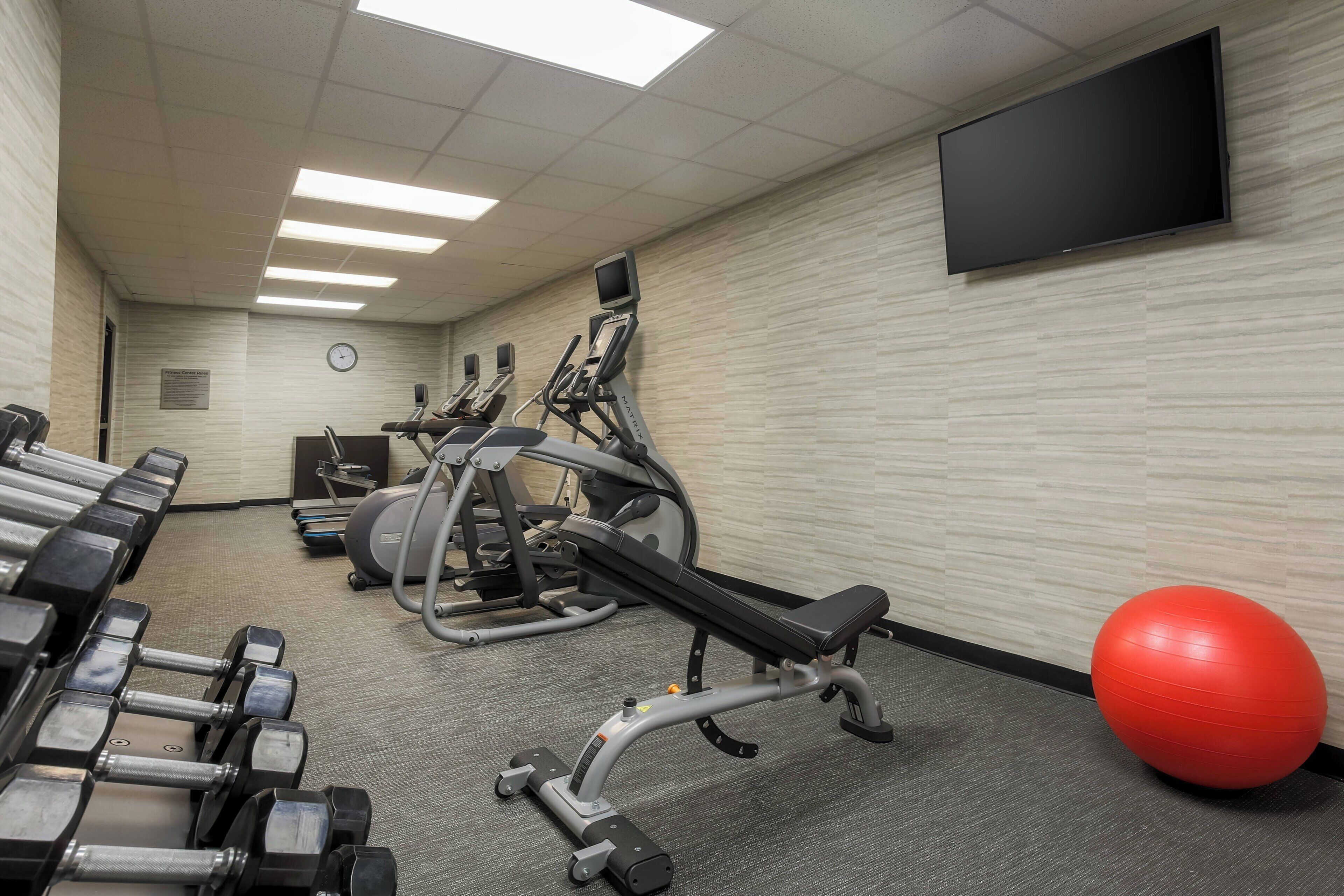A gym with exercise equipment, a television, and a clock on the wall.
