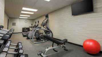 A gym with exercise equipment, a television, and a clock on the wall.