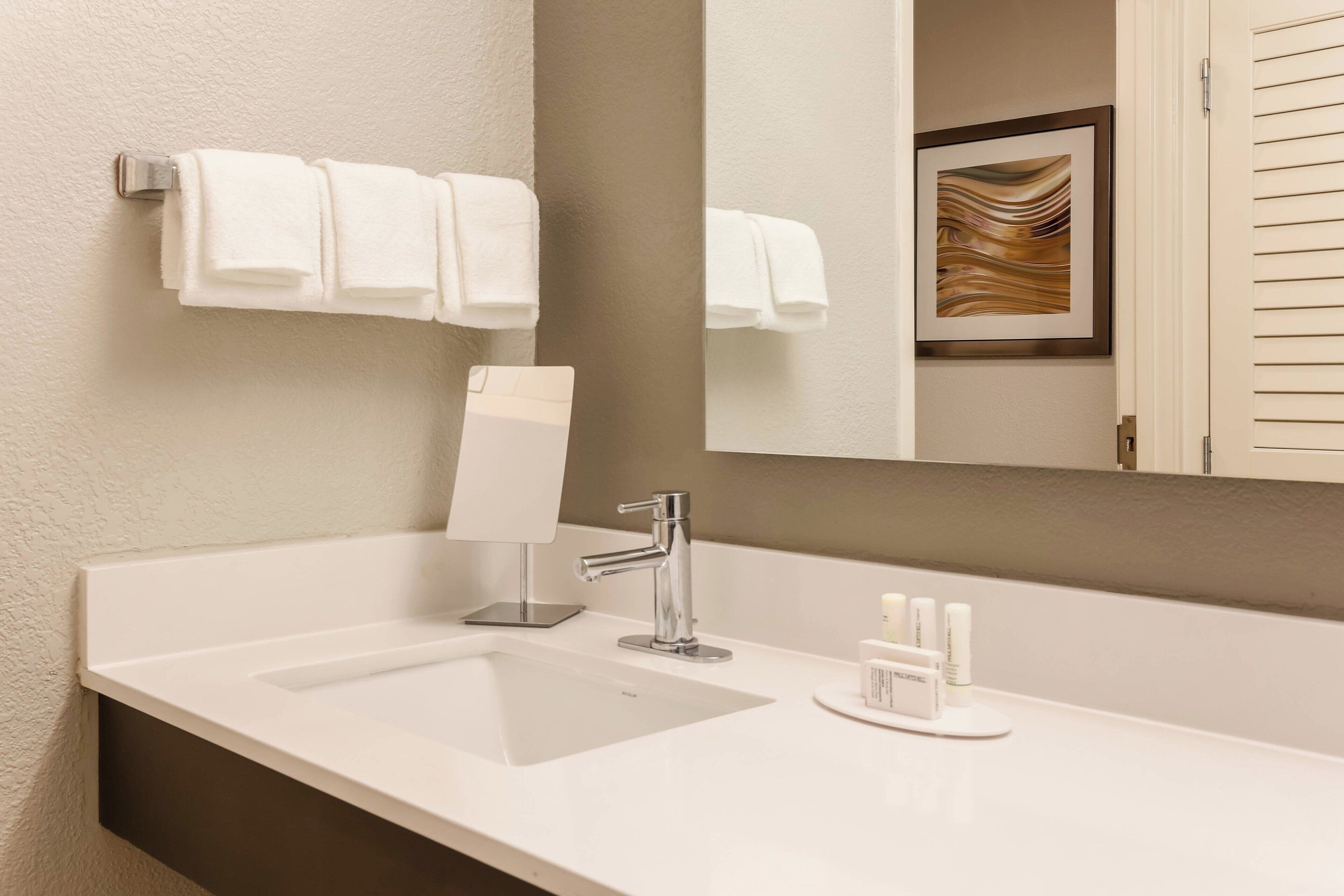 A modern bathroom with a white sink, a mirror, and two white towels hanging on a towel rack.