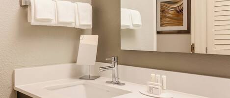 A modern bathroom with a white sink, a mirror, and two white towels hanging on a towel rack.