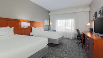 A hotel room with two beds, a desk, a chair, a television, and a window with curtains.