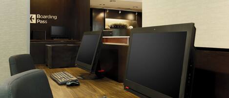 A modern office space with a wooden desk, two computer monitors, a keyboard, and a chair. A 'Boarding Pass' sign is visible on the wall.