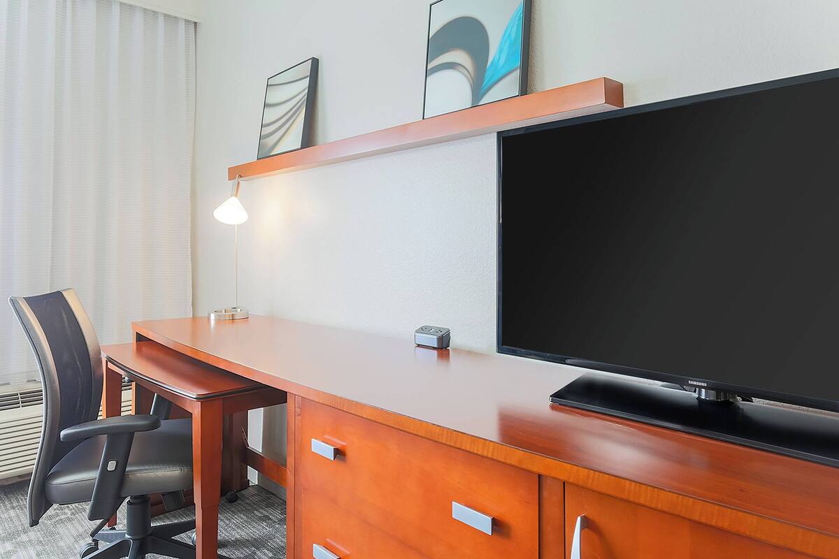 Ett hotellrum med ett skrivbord i trä, en tv, en stol och en lampa.