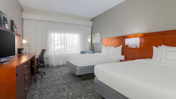 Habitación de hotel con dos camas, un escritorio con televisor, una silla y un ventanal con cortinas.