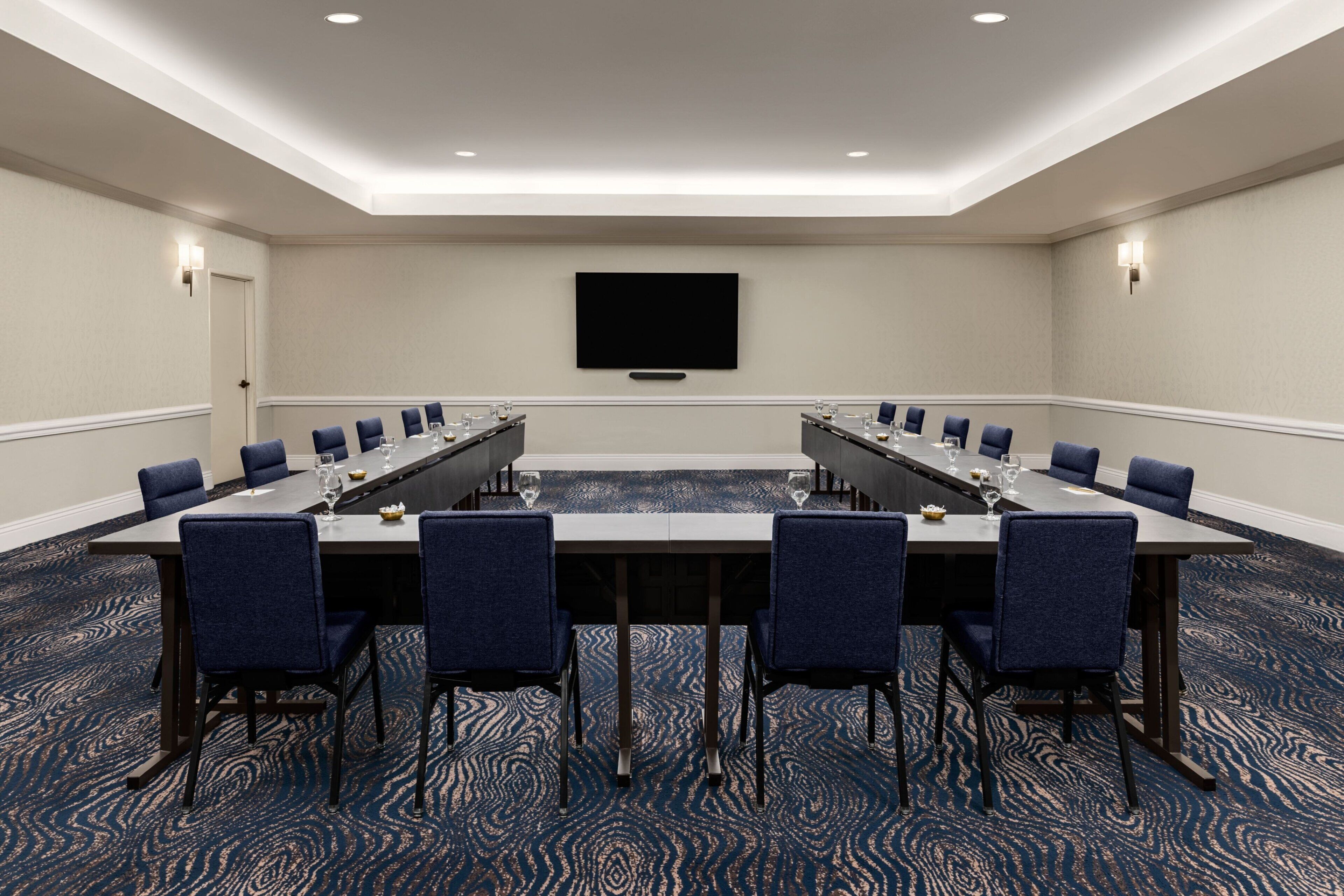A conference room with a long table, blue chairs, and a flat-screen TV on the wall.
