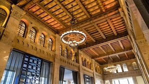 Un gran salón con techos de madera ornamentada, amplias ventanas de arco y una lámpara central.