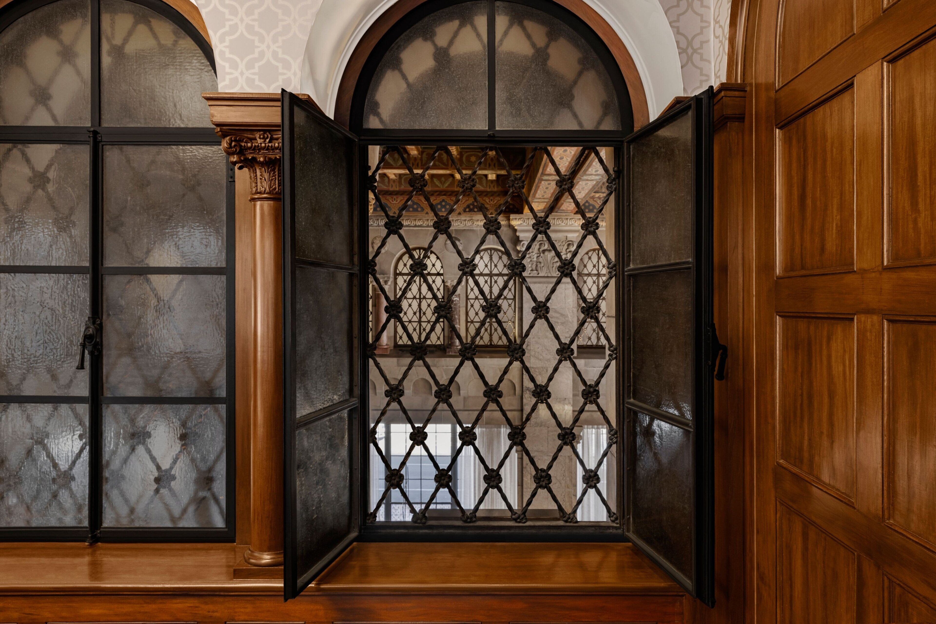Een kamer met een grote houten deur, een glazen scheidingswand met ruitmotief en uitzicht op een gedetailleerd interieur.